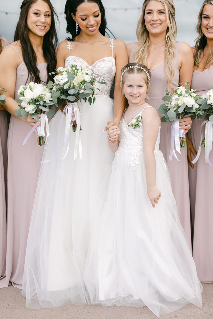 Bride and bridesmaids with bouquets of white flowers and greenery and flower girl in front