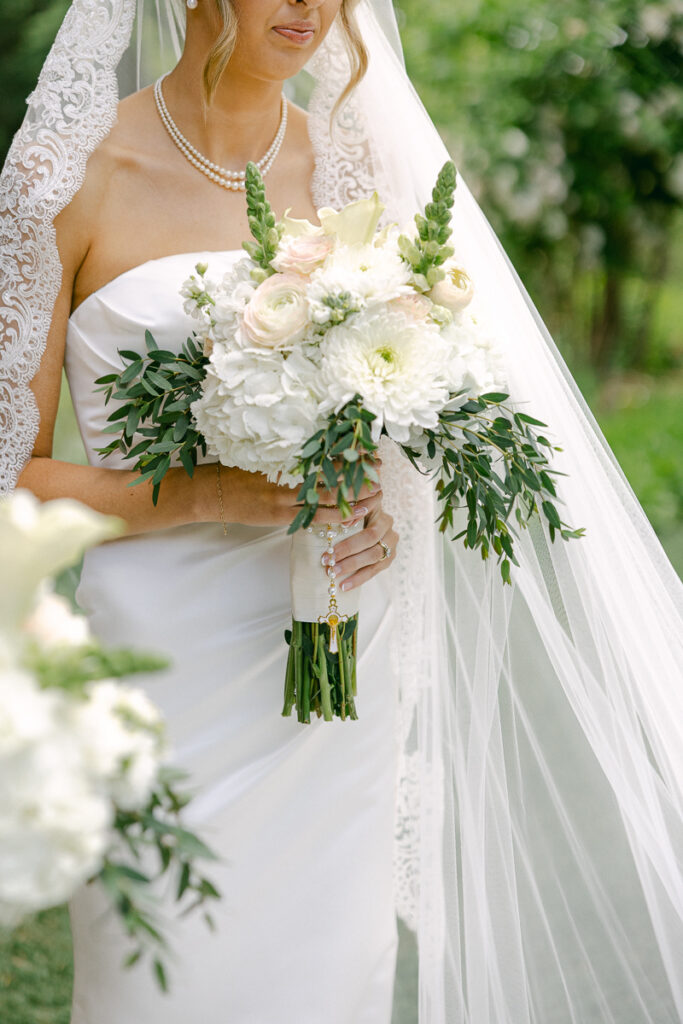 Emily and her bridesmaids laugh together holding white spring bouquets with sage green ribbons.