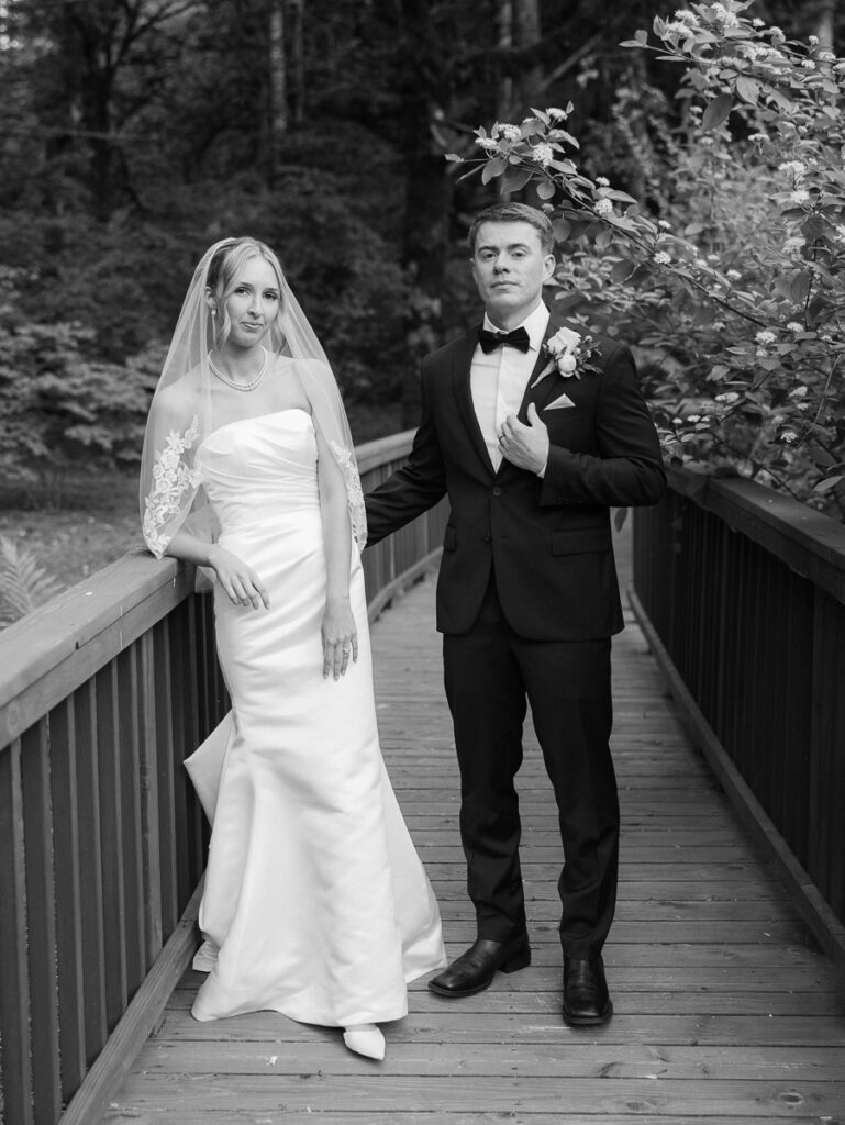 Black and white portrait of Owen and Emily in classic wedding attire on a wooden bridge in Oregon.